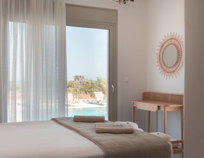 Een slaapkamer met een bed, een houten nachtkastje, een spiegel en uitzicht op een zwembad en groen.