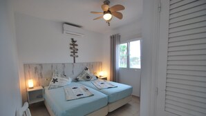 A bedroom with two beds, a ceiling fan, a nightstand, and a window with curtains.