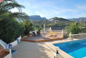 A poolside area with a view of mountains, a white fence, and a patio with chairs and umbrellas. - Marvious villa with private pool in quiet area (Calp)