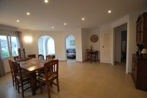 A spacious dining area with a large wooden table and chairs, a small side table, and a clock on the wall.