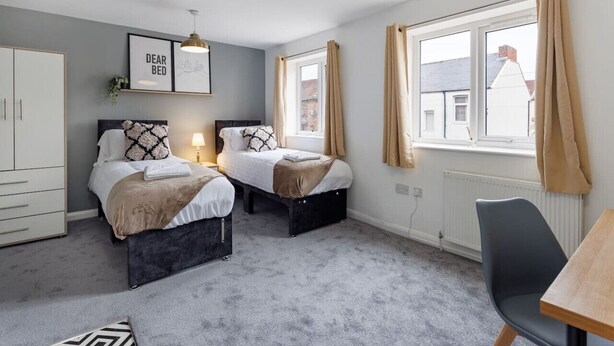 A bedroom with two beds, a wardrobe, a desk, and a window with curtains.