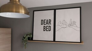 A framed artwork with the text "DEAR BED" and a line drawing of two hands holding each other.