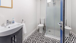 A bathroom with a white sink, two toilets, a shower with glass doors, and a patterned floor.