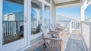 A covered outdoor deck with Adirondack chairs and a view of buildings in the background. - Fresh and Salty (Carolina Beach)