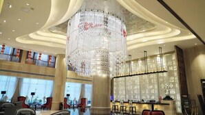 Un moderno vestíbulo de hotel con una araña central, zonas de estar y un mostrador de recepción.