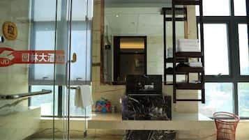 A hotel lobby with a glass door, a marble reception desk, a wooden shelf with towels, and a large window.