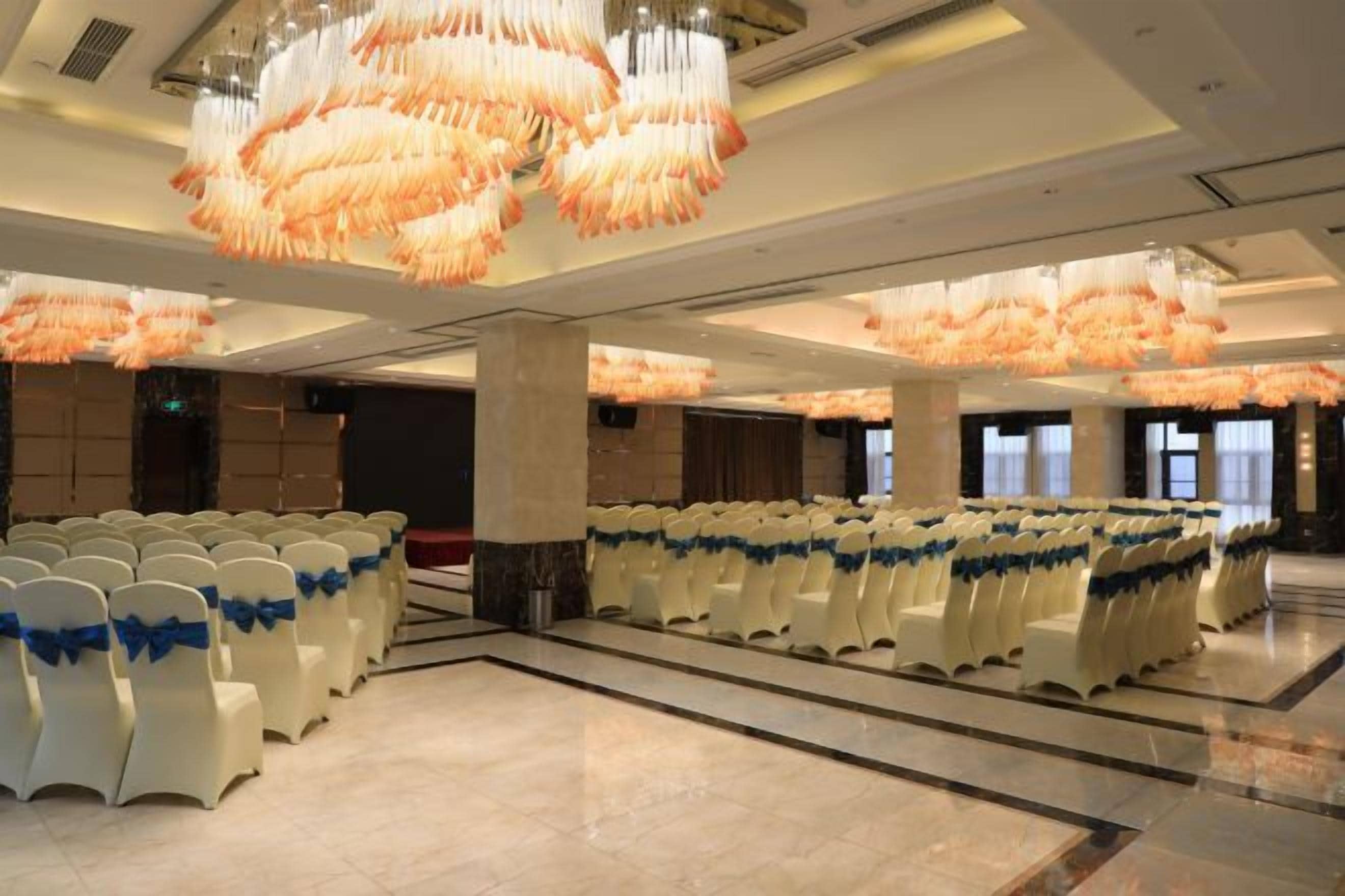 A spacious hall with rows of white chairs, large chandeliers, and a polished floor.