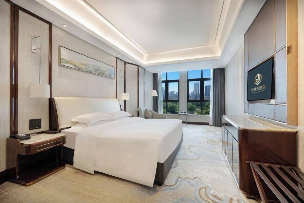 A modern hotel room with a large bed, a desk, a TV, and a city view.