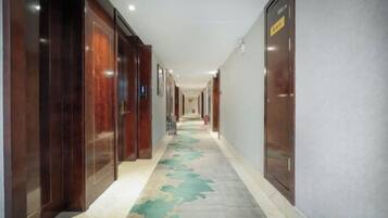 A hotel corridor with wooden doors, a patterned carpet, and a wall-mounted elevator.