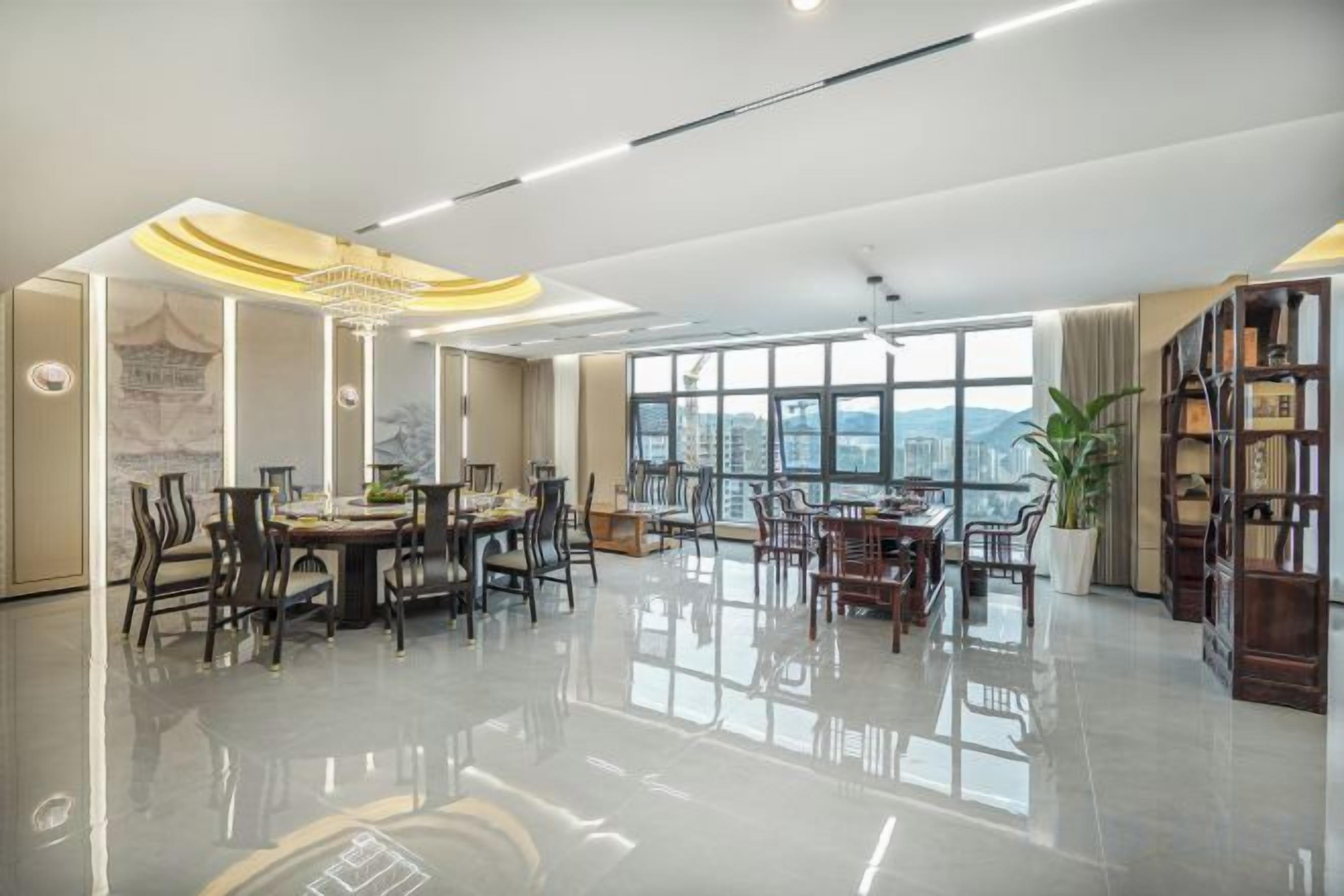 A spacious room with a dining area, a large window with a city view, and a bookshelf.
