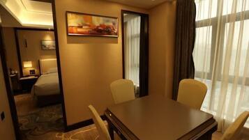 A hotel room with a bed, a desk, and a chair. There is a painting on the wall and a window with curtains.