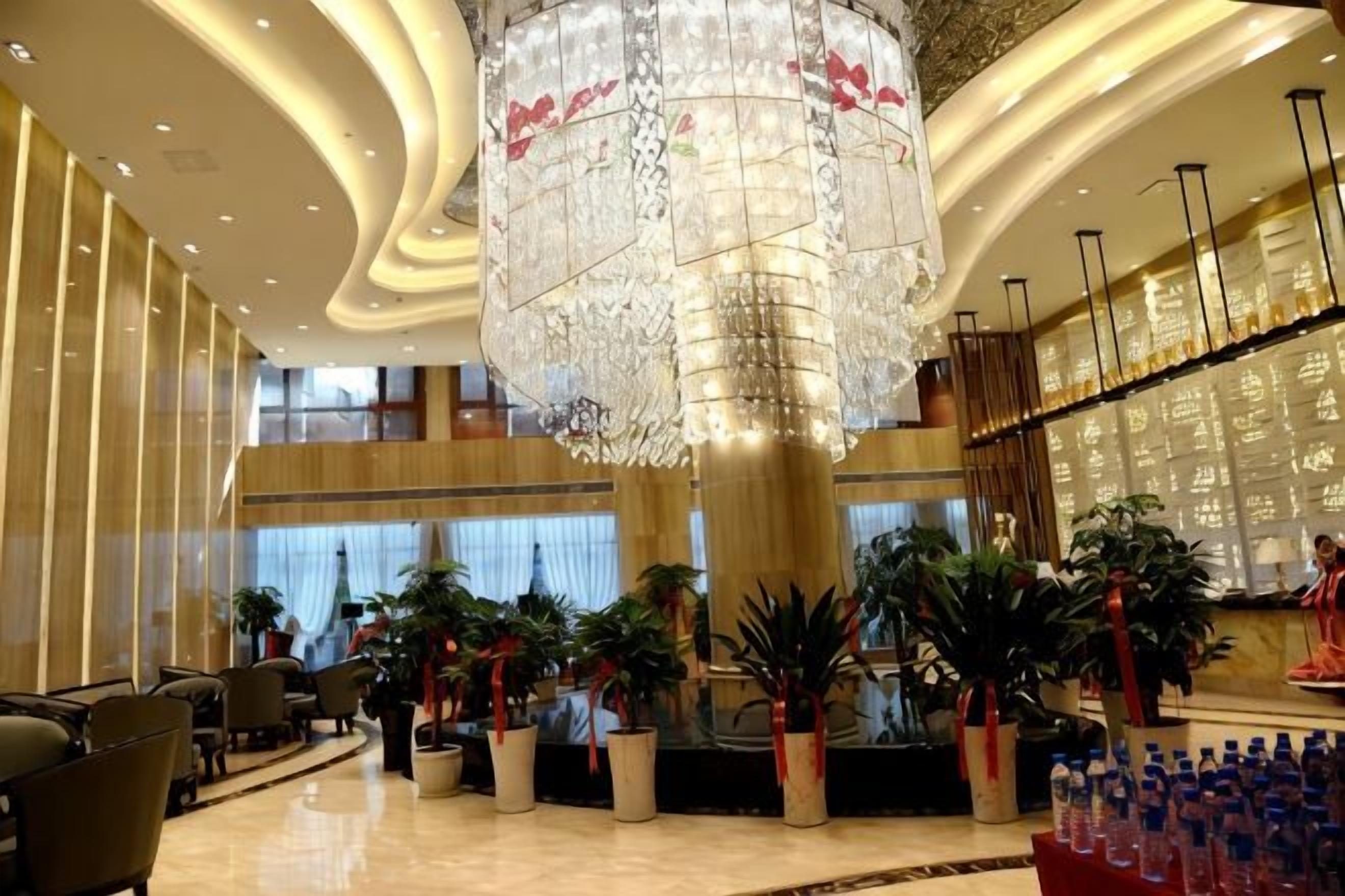 A spacious lobby with a large chandelier, multiple seating areas, and potted plants.