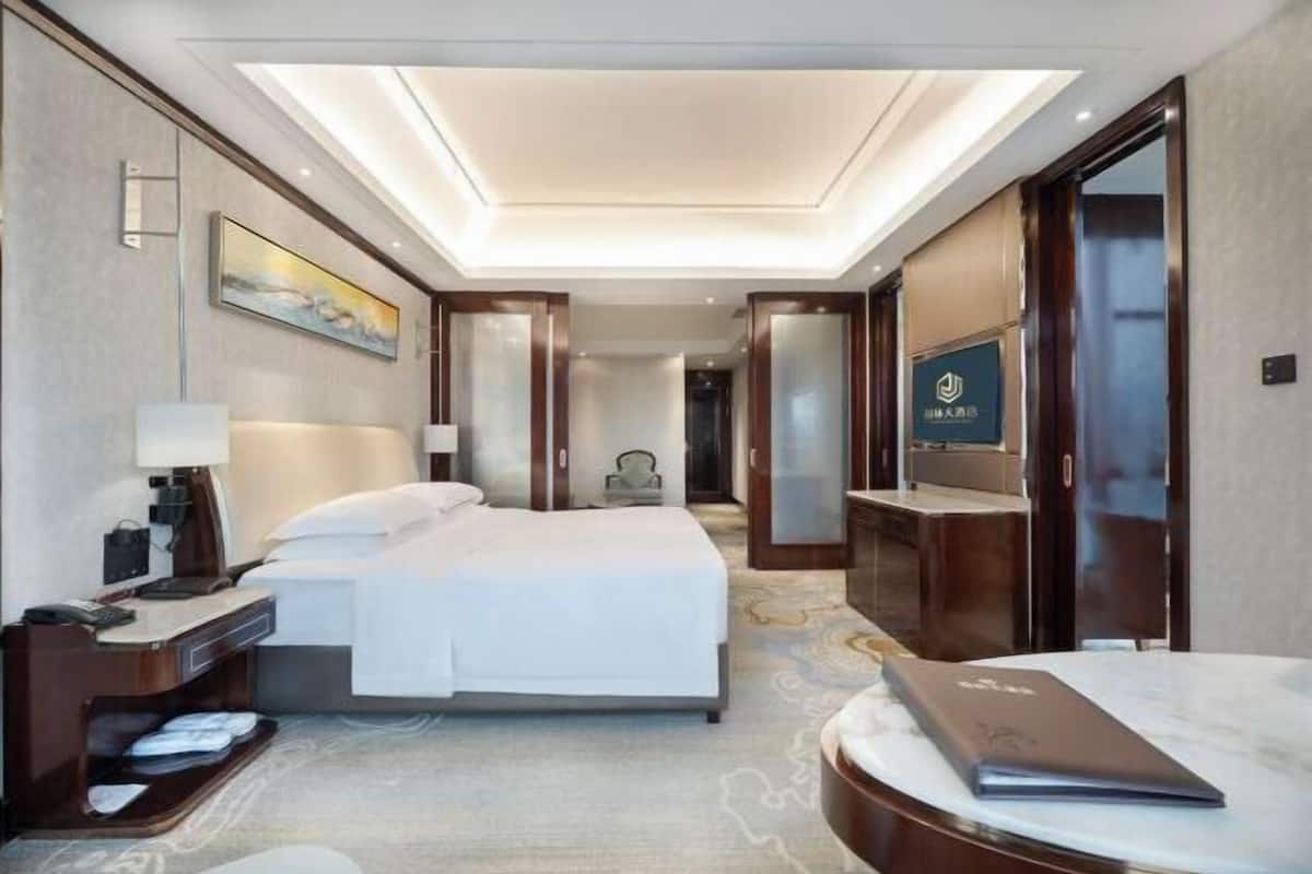 A hotel room with a large bed, a desk with a lamp, a TV, and a minibar.