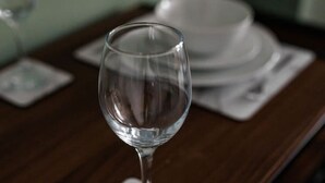 Una mesa de comedor con una copa de vino sobre un posavasos, platos apilados al fondo y un mantel individual de mármol.