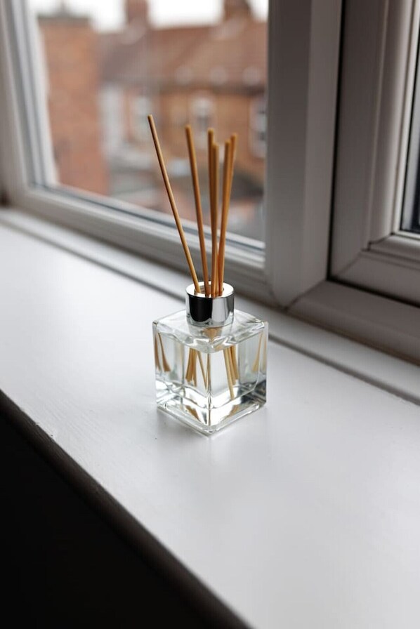 Une bouteille en verre transparent avec des bâtonnets en bois, posée sur un rebord de fenêtre.
