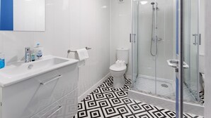 Un baño moderno con ducha de vidrio, un lavamanos blanco con espejo y piso estampado.
