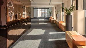 Un pasillo moderno con paredes reflectantes, alfombra estampada, bancos de madera y plantas en macetas.