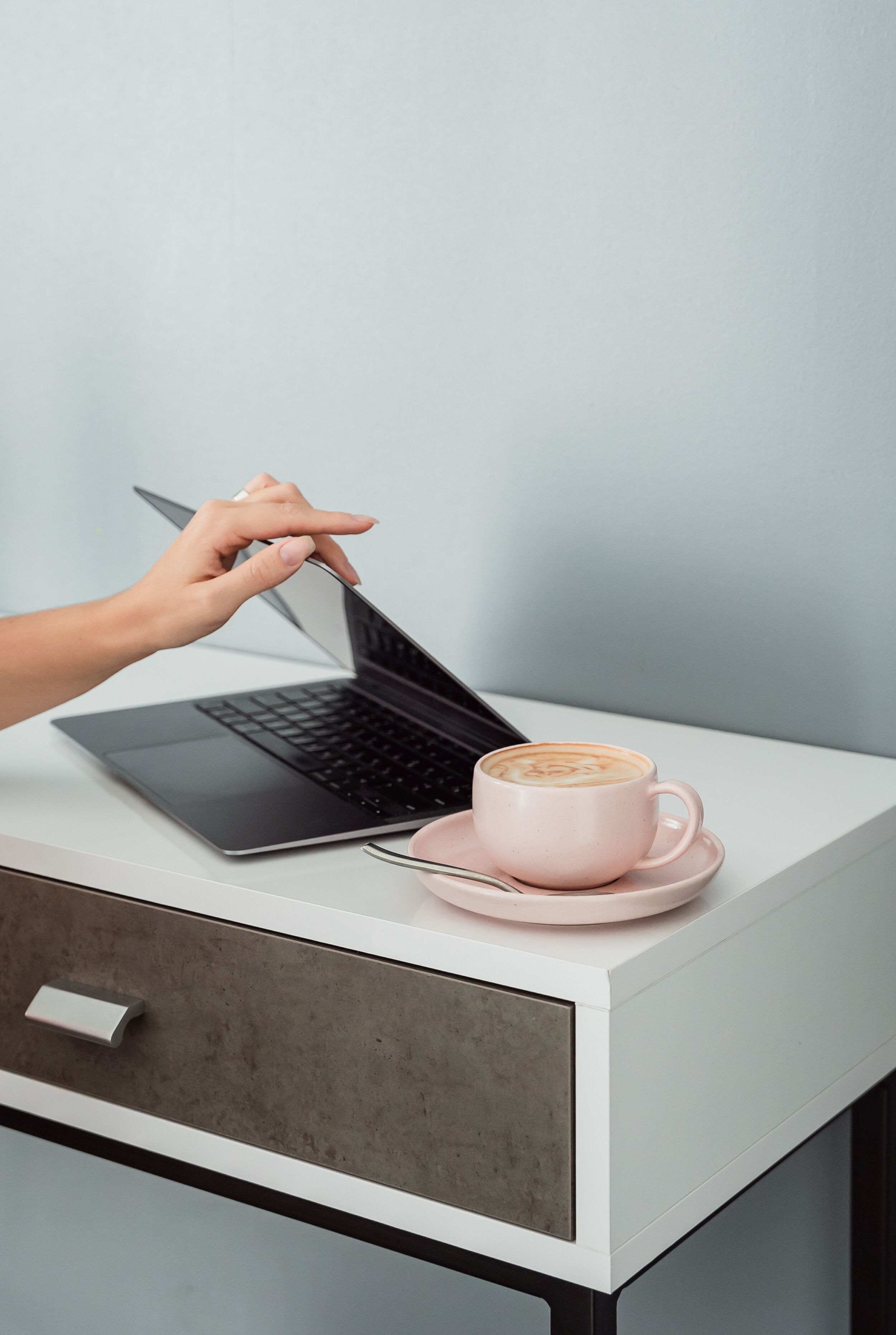 Een laptop op een wit bureau met een roze koffiekop en een lepel.