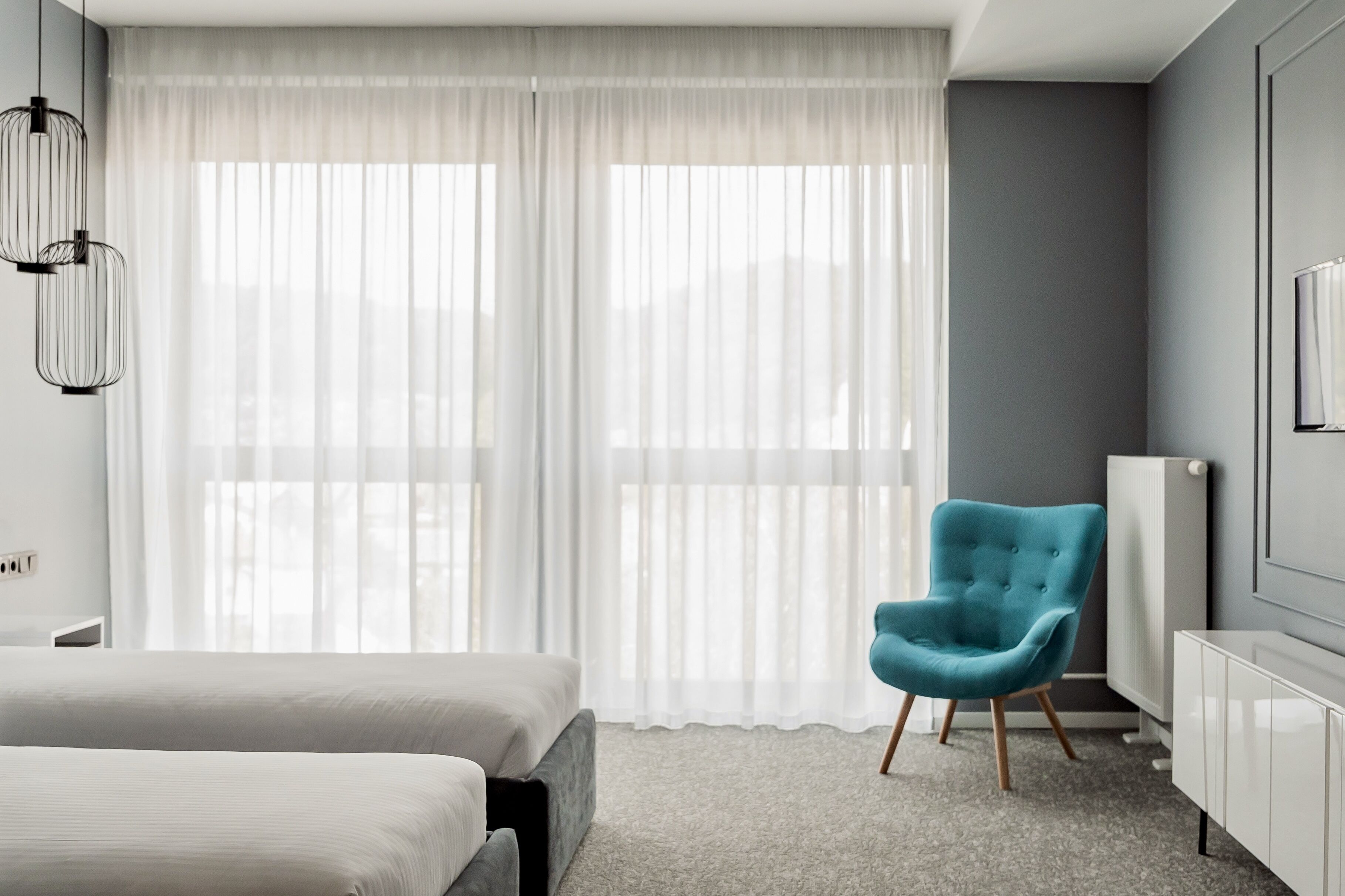 A modern hotel room with a large bed, a blue armchair, and a white radiator.