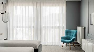 A modern hotel room with a large bed, a blue armchair, and a white radiator.