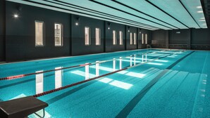 Una piscina interior larga con carriles bien definidos, suelo de baldosas y una serie de ventanas a lo largo de una pared.