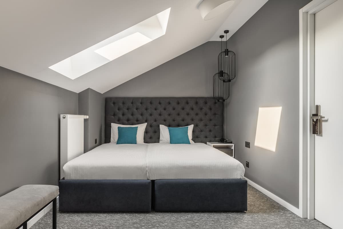 Un dormitorio moderno con una cama grande, un banco, un tragaluz y una mesita de noche.