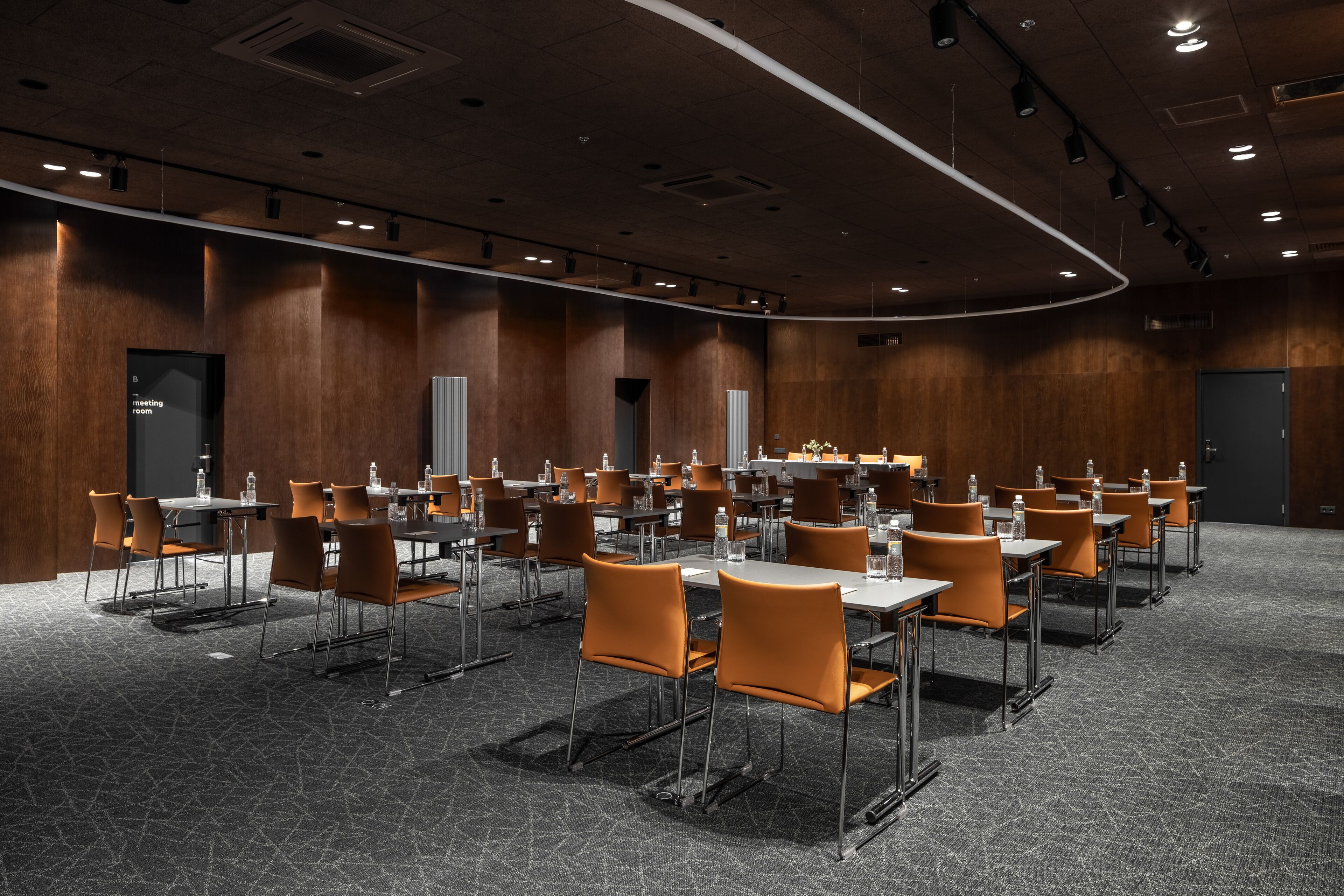 A conference room with rows of tables and chairs, equipped with water bottles.