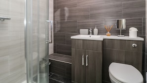 Ein modernes Badezimmer mit einer Duschkabine aus Glas, einem Waschbecken inklusive Spiegel und einer Toilette.