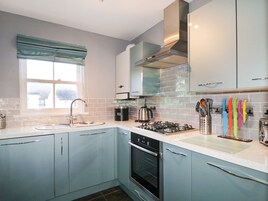 A modern kitchen with light blue cabinets, a stainless steel range hood, a gas stove, and a window with blue curtains.