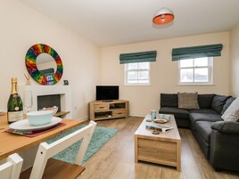 A modern living room with a wooden coffee table, a grey sofa, a television, and a colorful circular mirror.