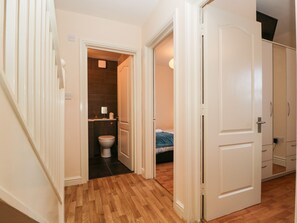 Een gang met een houten vloer, die leidt naar een badkamer en een slaapkamer.