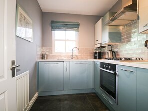 Een keuken met lichtblauwe kastjes, een raam met een blauwe gordijnboog, een roestvrijstalen afzuigkap en een inbouwoven.