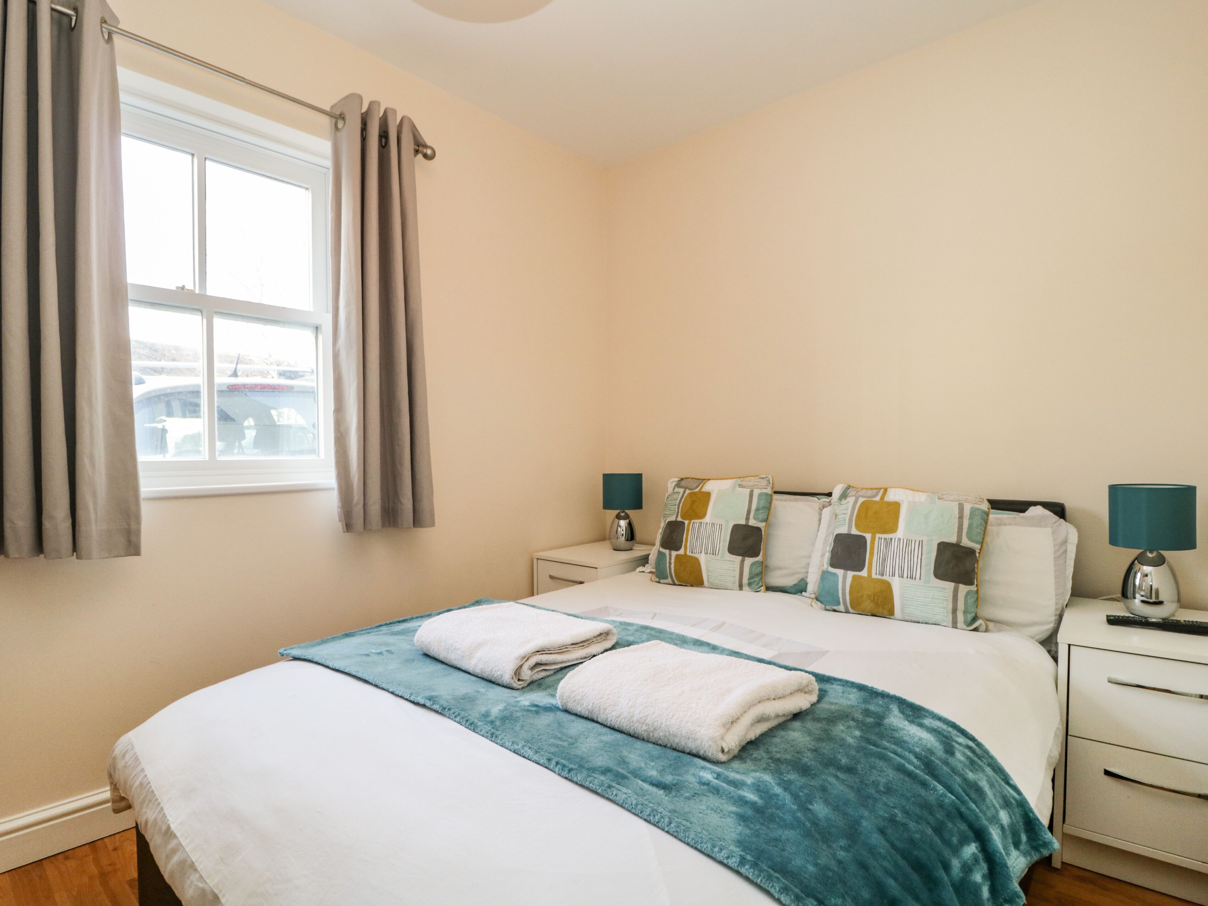 A bedroom with a bed, two bedside tables, a window with curtains, and a view of a bridge.
