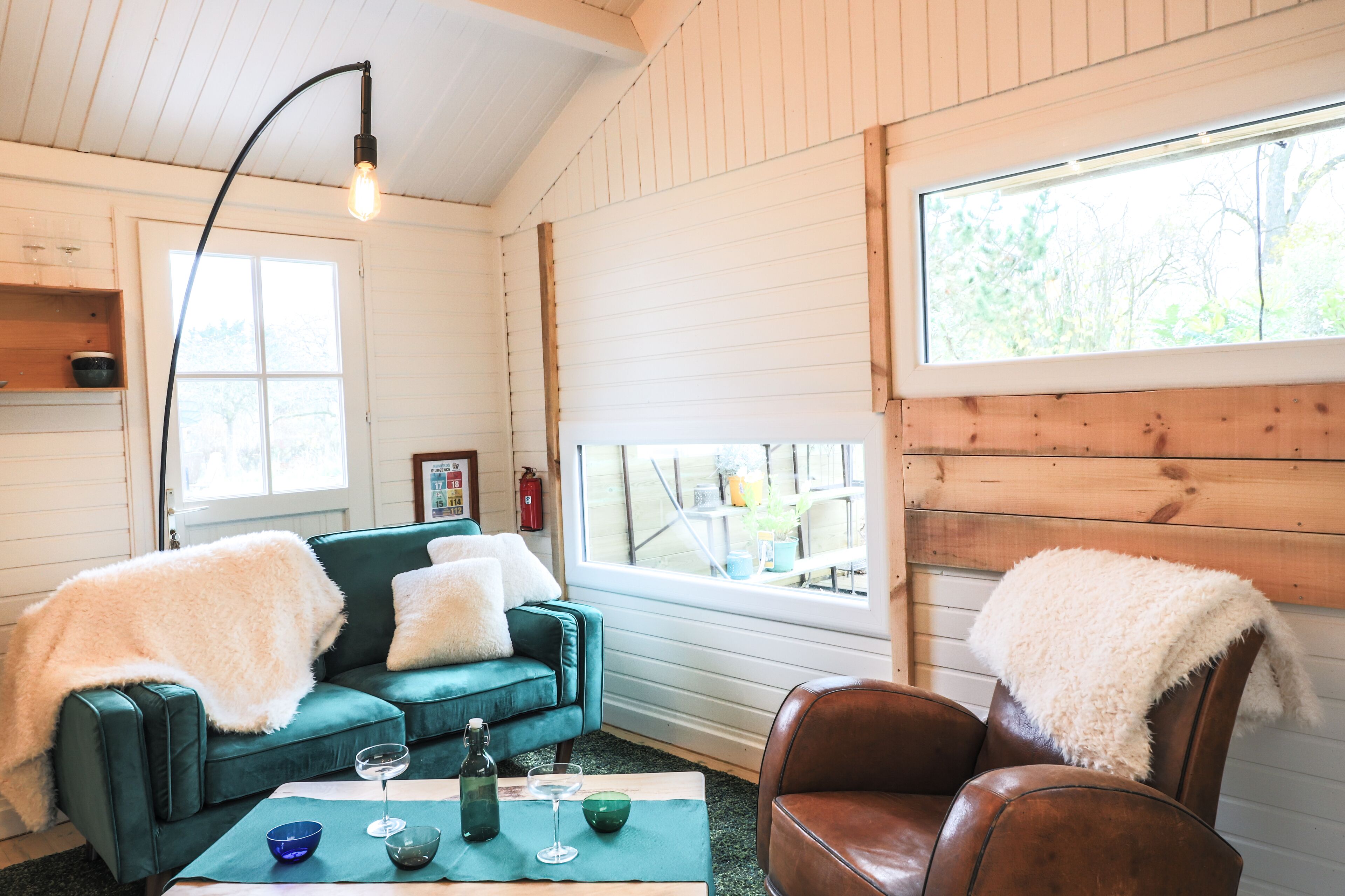 A cozy room with a green sofa, a brown leather chair, and a table with a bottle and glasses.