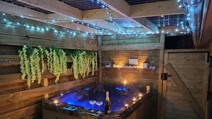 Un intérieur en bois agrémenté d’un jacuzzi, de guirlandes lumineuses et de plantes suspendues.