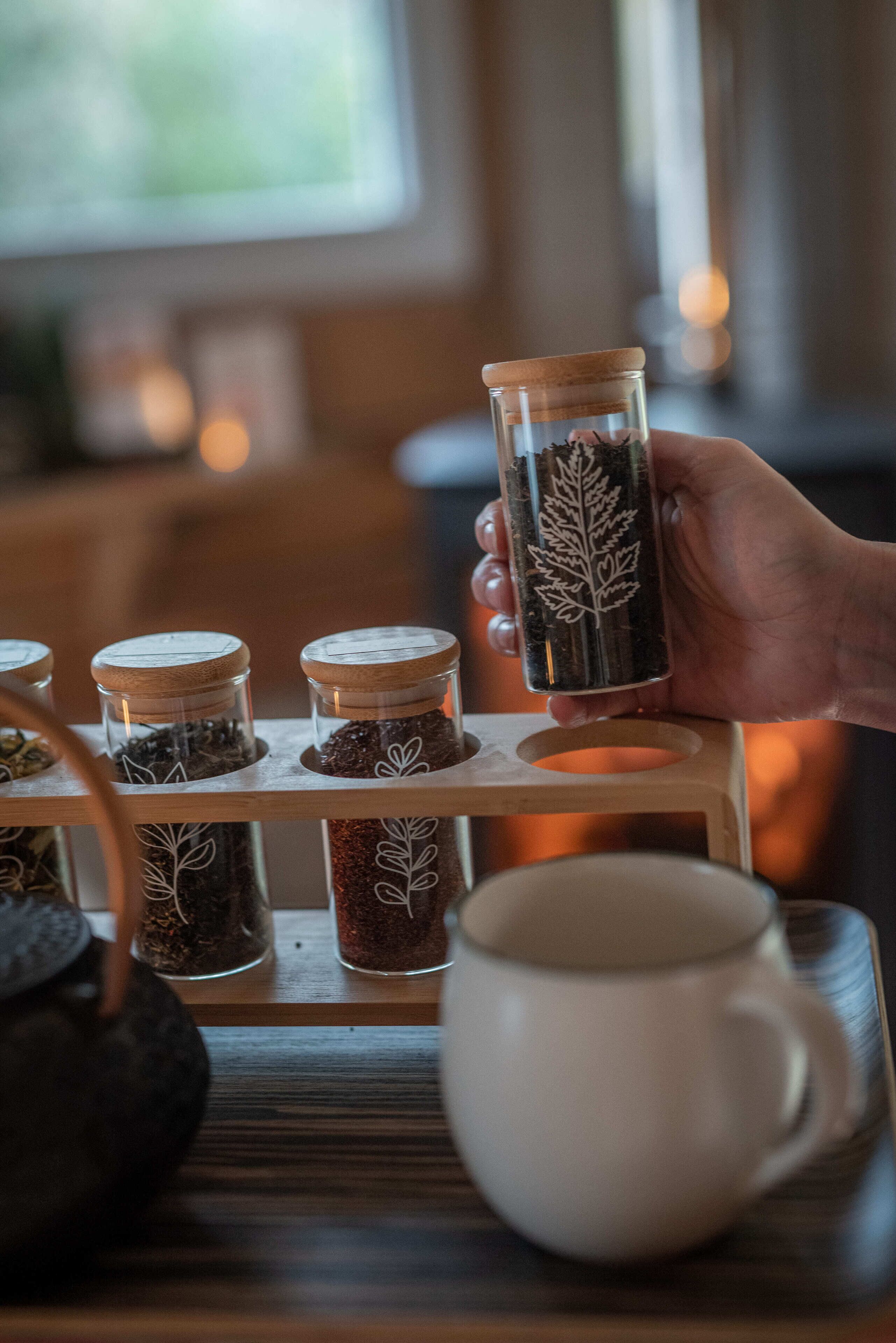 A hand holding a jar with a leaf design, with other jars on a wooden stand.