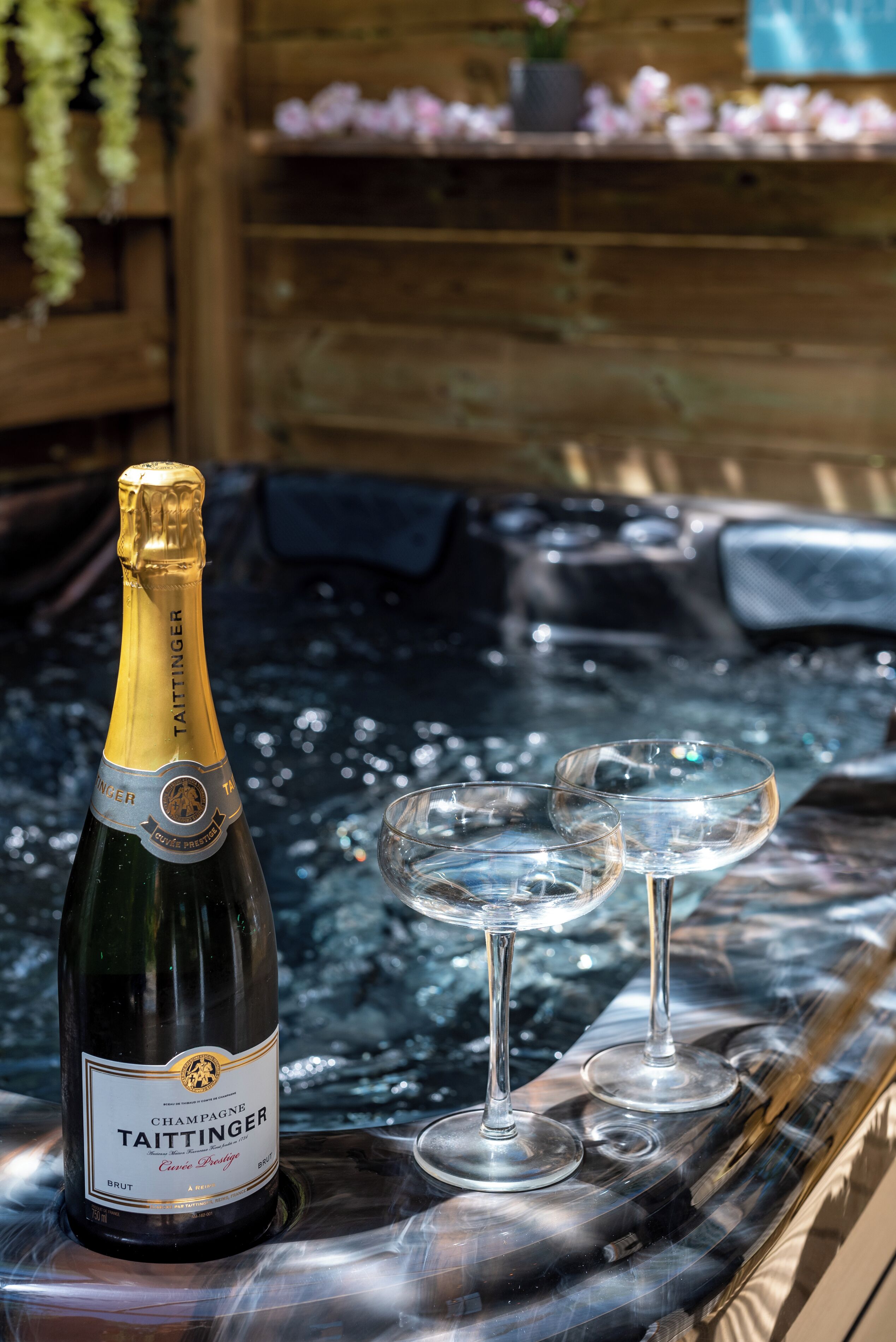 A bottle of Taittinger champagne and two glasses on a reflective surface.