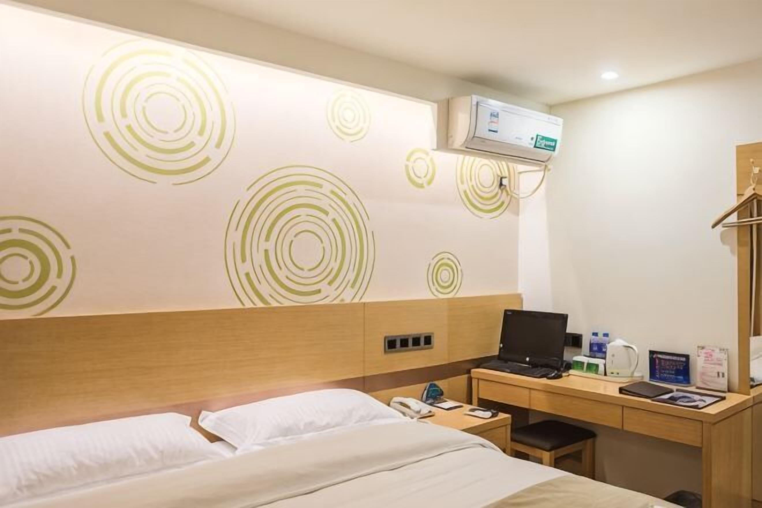 A hotel room with a bed, desk, and wall-mounted air conditioner.