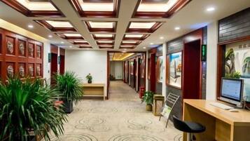 Un hall de hotel con mostrador de recepción, zona de estar y un largo pasillo con alfombra estampada.