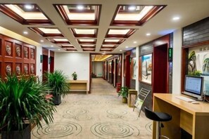 Una hall d'albergo con reception, area salotto e lungo corridoio con tappeto decorato.