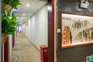 A hotel corridor with a carpeted floor, a framed artwork on the wall, and a red trash bin.