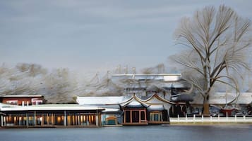 A waterfront building with traditional architecture, a large tree, and a snow-covered landscape.