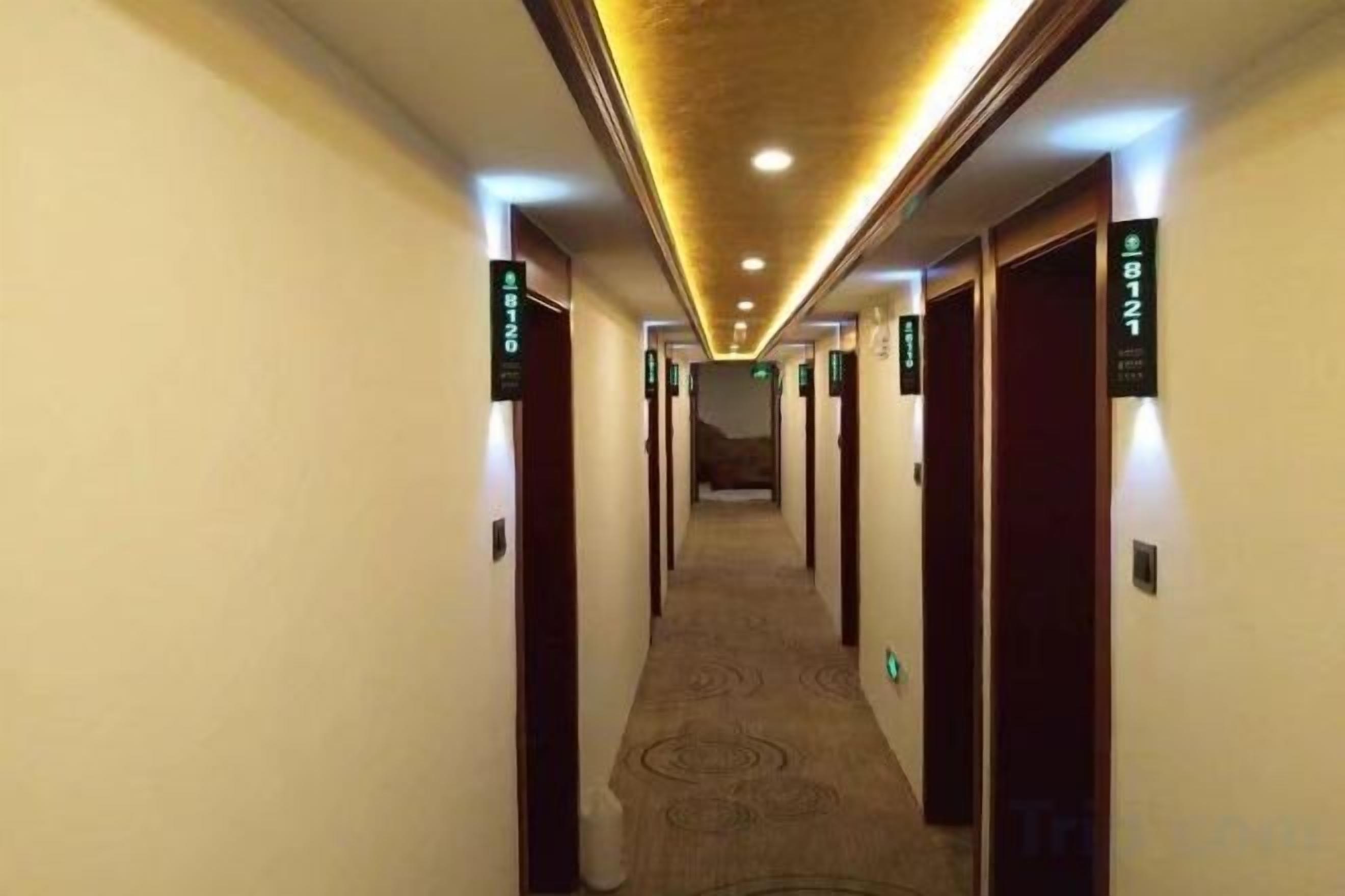 Un pasillo de hotel con puertas numeradas, piso alfombrado e iluminación en el techo.