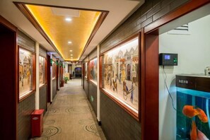 Un corridoio di un hotel con opere d'arte incorniciate alle pareti, un acquario con pesci arancioni e un cestino della spazzatura rosso.