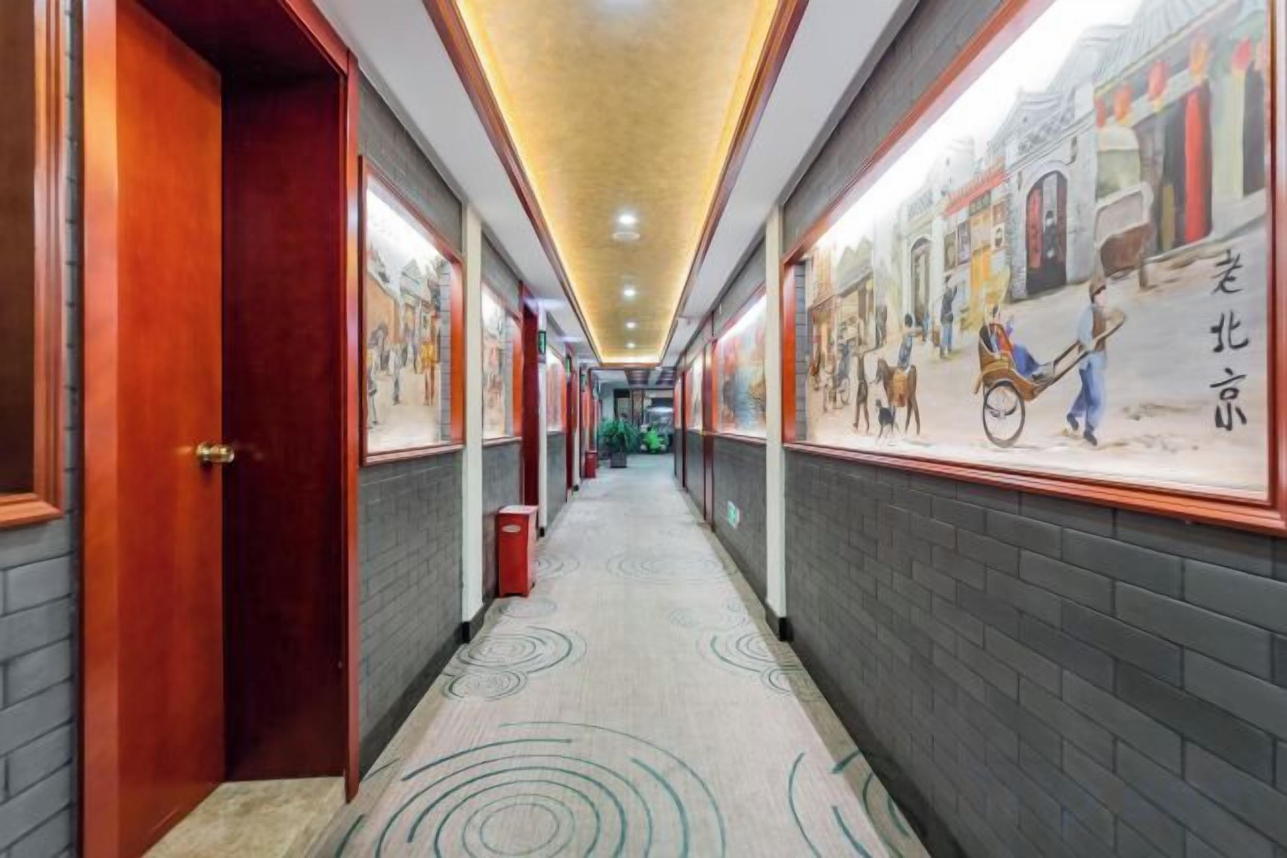 A corridor with doors on the left, a patterned floor, and wall murals depicting traditional scenes.