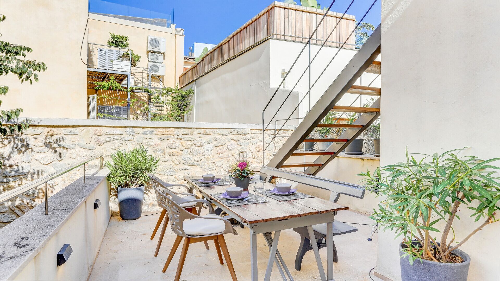 An outdoor dining area with a table and chairs, a stone wall, and a staircase.