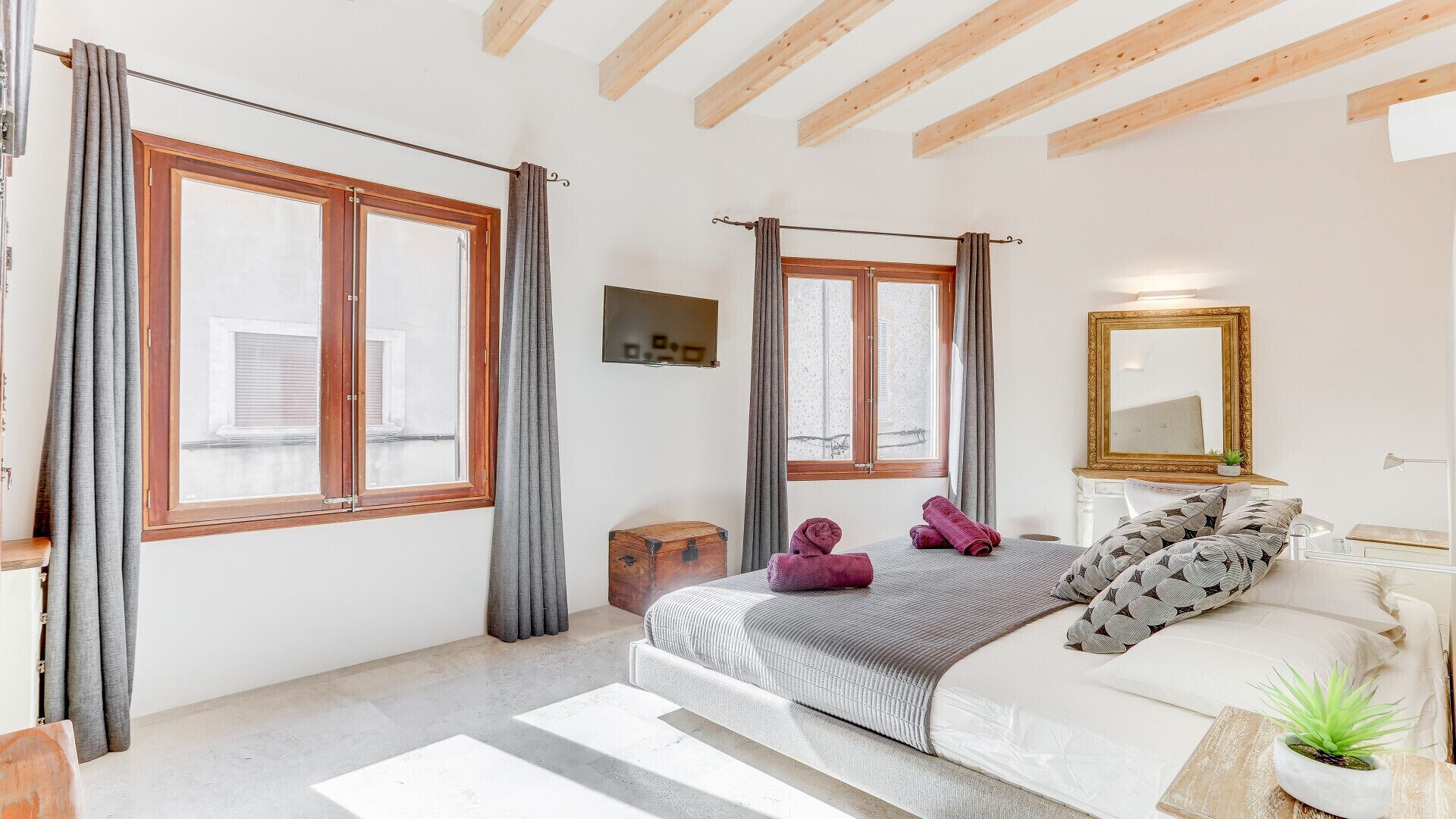 Een slaapkamer met een groot bed, een nachtkastje, een spiegel en een raam met gordijnen.