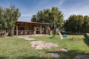 A rustic outdoor patio with a stone building, a slide, and a small play area.