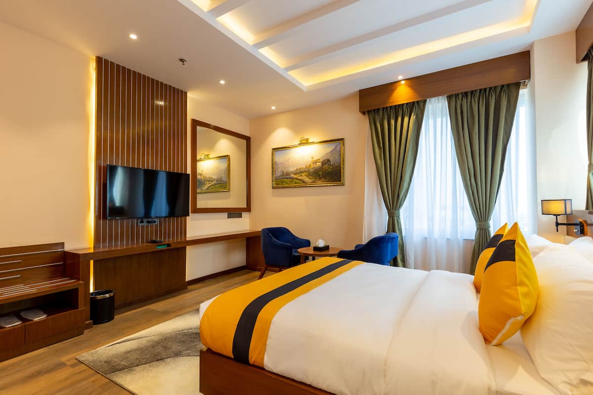 A hotel room with a large bed, a flat-screen TV, a desk, and a seating area with chairs.
