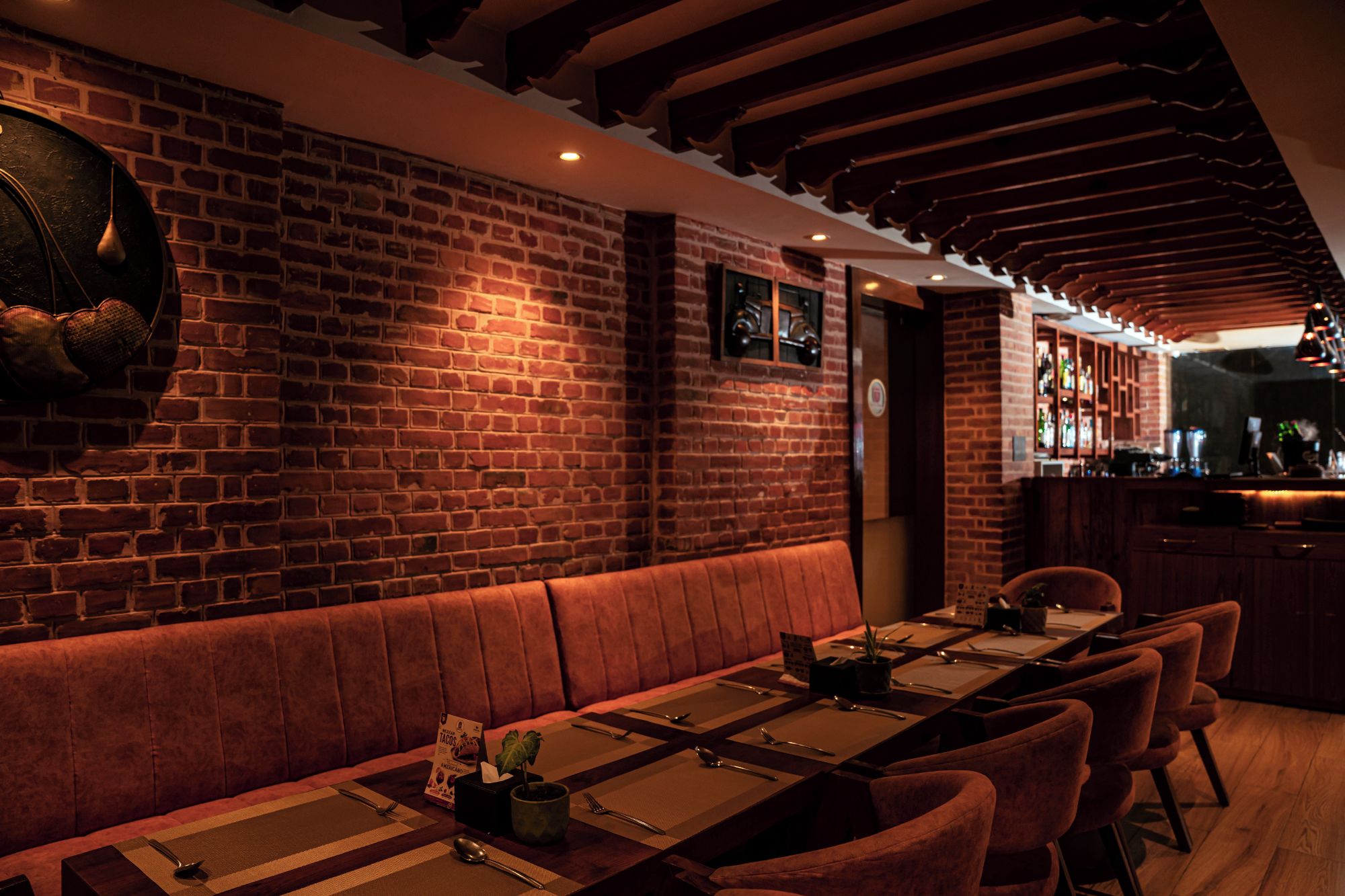 Un restaurante con paredes de ladrillo, vigas de madera en el techo y una zona de bar.